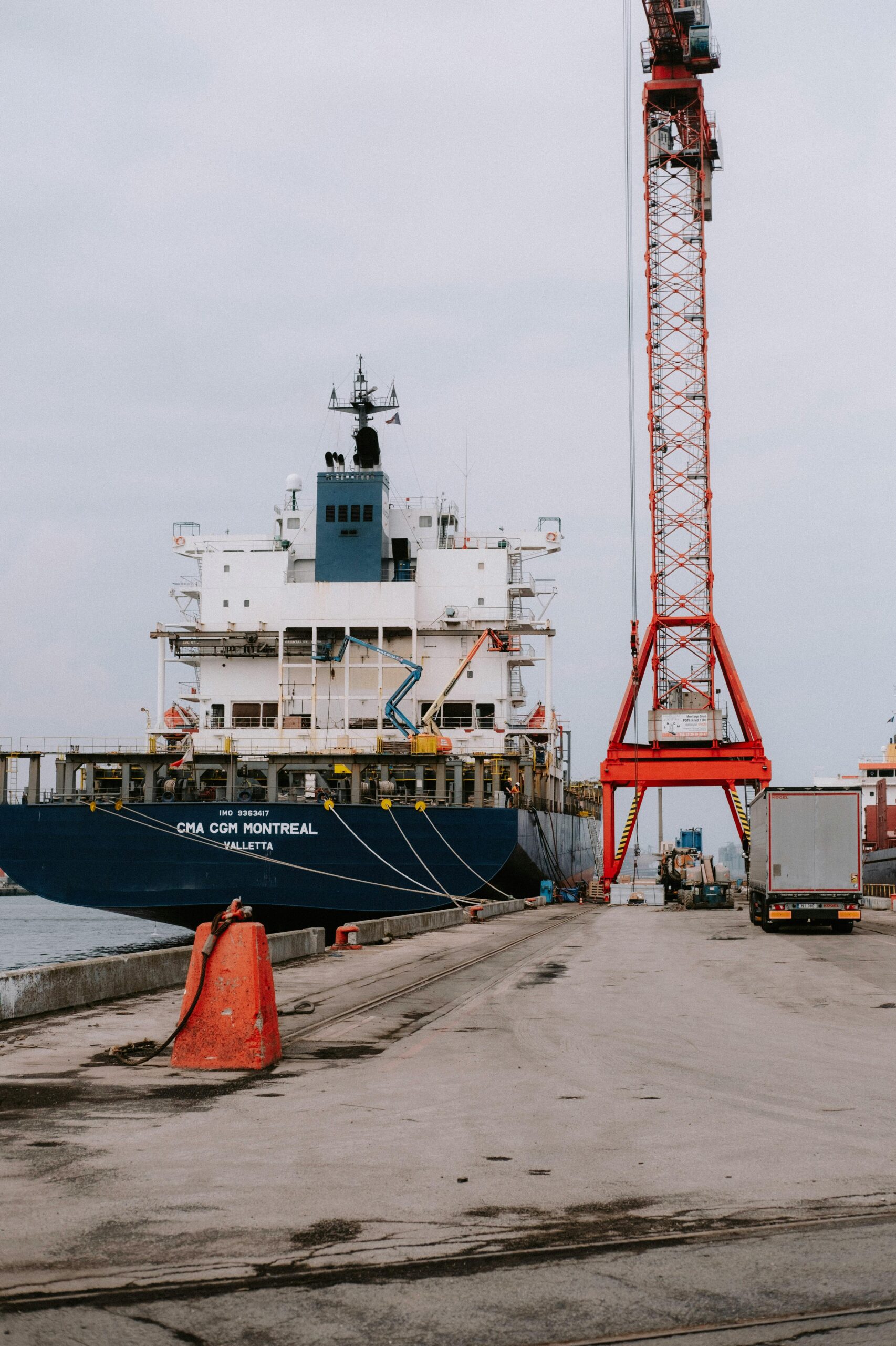 Container ship at a bustling port with cranes and trucks in view.